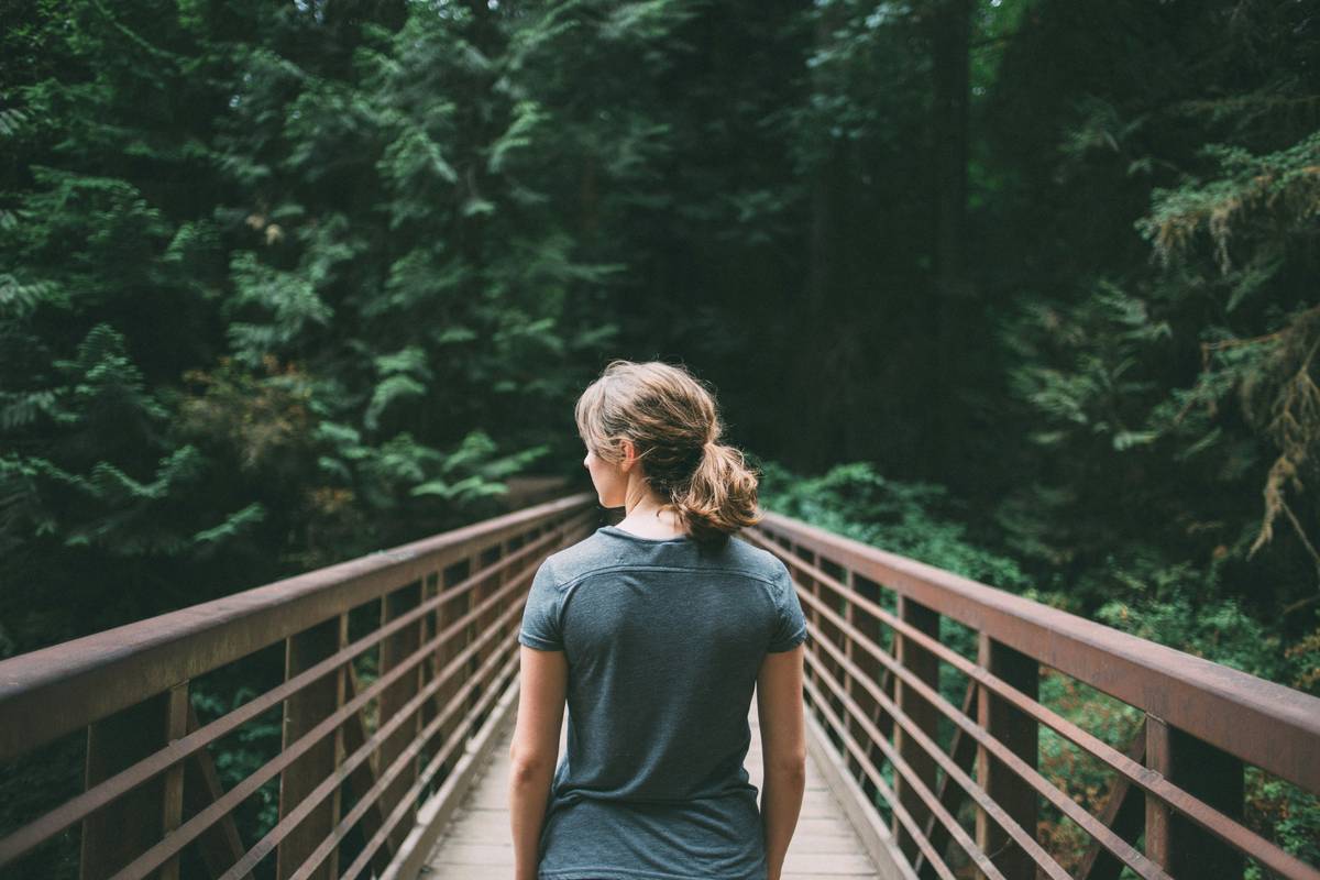 Someone walking alone across a footbridge into a quiet forest — a private moment of working through a decision.
